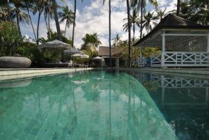 a swimming pool with blue water and palm trees at Villa Pantai Matanai in Tianyar
