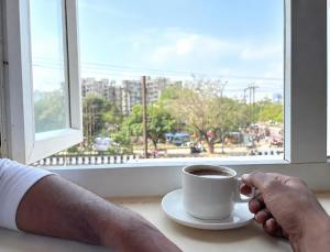 a person holding a cup of coffee in front of a window at Hotel West Residency Delhi Airport in New Delhi