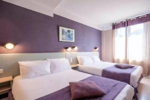 two beds in a hotel room with purple walls at Hôtel Christina Lourdes in Lourdes