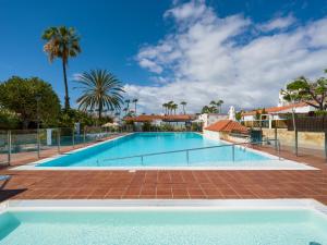 a large swimming pool with a fence and palm trees at Oasis Beach Holiday Home with jacuzzi in Playa del Ingles