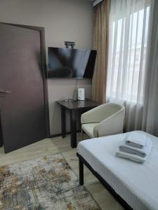 a room with a bed and a desk and a television at Hotel Mansuri in Almaty
