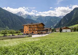 a large building in a field with mountains in the background at Sidan Hotel Restaurant & Pizzeria in Schwendau