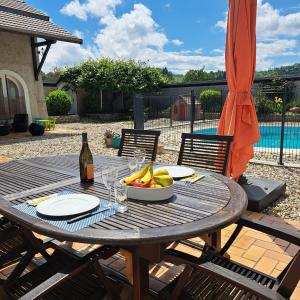a table with a bowl of fruit and a bottle of wine at Charmante maisonnette avec piscine partagée in Charancieu