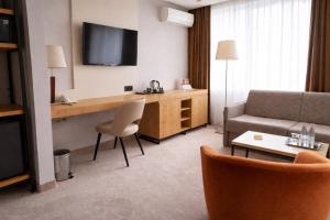 a hotel room with a couch and a desk with a television at Hotel Kudowa Manufaktura Relaksu in Kudowa-Zdrój