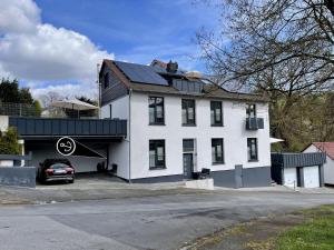 a white house with a car parked in a parking lot at Fewo Diemelsee 1 in Heringhausen