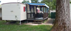 a white house with a porch next to a tree at le 130 mobile home à Meschers sur Gironde au camping L'escale in Meschers-sur-Gironde