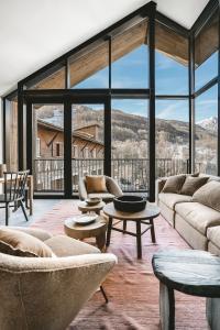 a living room with couches and tables and large windows at Les Chalets du Grand Hôtel in Saint-Chaffrey