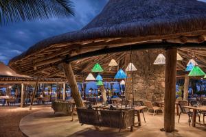 a restaurant with a straw roof and tables and chairs at Heritage The Villas in Bel Ombre