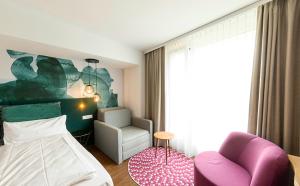 a bedroom with a bed and a chair at DORMERO Hotel Freiburg in Freiburg im Breisgau
