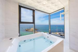 a bath tub in a bathroom with a view of the ocean at Gangneung Dolgorae Spa Pension in Gangneung
