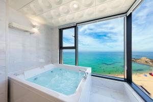a bath tub in a room with a view of the ocean at Gangneung Dolgorae Spa Pension in Gangneung
