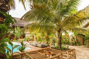 ein tropischer Garten mit einer Couch unter einer Palme in der Unterkunft Oke Ani Boutique Hotel in Paje