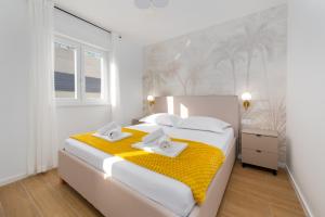 a white bedroom with a large bed with yellow blanket at Lejla Garden Apartment in Podstrana
