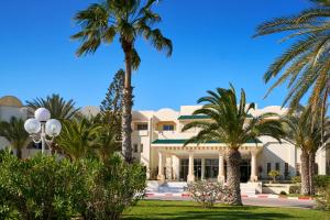 a large white house with palm trees in front of it at Medina Les Quatre Saisons Aqua Park Resort and Thalasso Djerba in Djerba