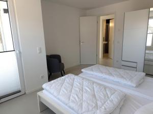 a white bedroom with two beds and a chair at Haus am Wittenwiewerbarg in Dahme