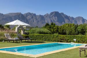 a pool with chairs and an umbrella with mountains in the background at La Cabriere Country House in Franschhoek