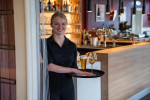 a woman holding a tray with a glass of wine at Hotel Oepkes in West-Terschelling