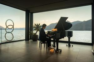 a man playing a piano in front of a large window at Relais Villa Porta in Luino +89 photos
