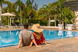 a man and woman sitting next to a swimming pool at La Finca Resort in Algorfa