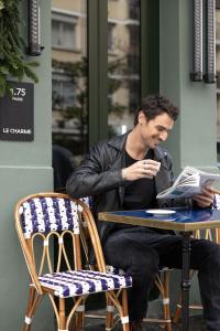 a man sitting at a table reading a newspaper at 1.75 Paris Le Charme in Paris