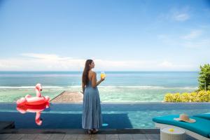 a woman standing on the edge of a pool with a drink at Nusa Dua Cliff Ocean View with Private Beach in Nusa Dua