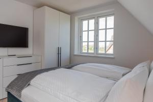 a white bedroom with a bed and a television at Reetruhe in Borgsum