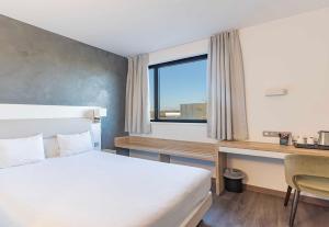 a bedroom with a bed and a desk and a window at B&B HOTEL Brumath Bernolsheim in Brumath
