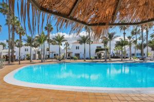 a swimming pool with palm trees and buildings at Casa Oasis in Corralejo