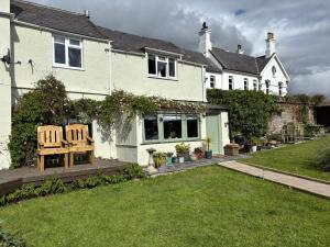 a house with two wooden chairs in the yard at Cottage Sleeps 4 with Wifi in Llanfairpwllgwyngyll