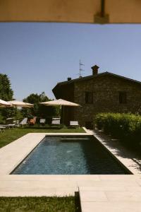 a swimming pool in front of a house with umbrellas at Cascina Belvedì in Clanezzo