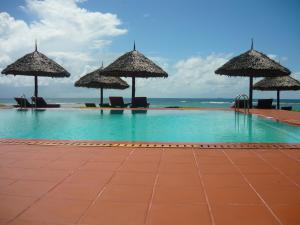 a swimming pool with umbrellas and the ocean at Amani Beach Resort in Dar es Salaam