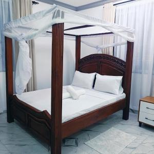 a wooden canopy bed with white sheets and pillows at Summer Malindi Family House in Malindi