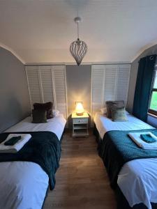 two beds in a room with a lamp on a table at Woodside Lodge, Weybourne, Holt in Weybourne