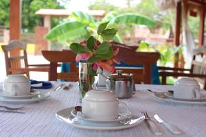 a table with plates and a vase with flowers on it at Pousada Paraíso dos Ipês in Jijoca de Jericoacoara