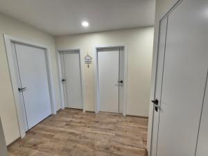 an empty hallway with three doors and wood floors at MV Apartament in Druskininkai