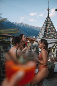 three women in orange bathing suits drinking drinks on a balcony at Vitalpina Hotel Schulerhof in Plaus