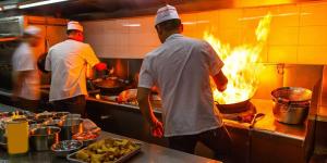 three men in a kitchen preparing food on a stove at Hotel Tirreno in Lavagna