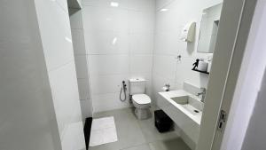 a white bathroom with a toilet and a sink at Hotel Moriah in Umuarama