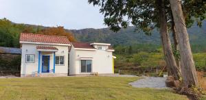 a small white house in a field with a tree at Full Moon Dalbawi Pension in Jangheung