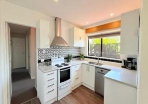 a white kitchen with white cabinets and a window at Stylish Trentham Retreat in Upper Hutt