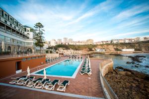 a beach with a pool, chairs, and a balcony at Vila Gale Ericeira in Ericeira