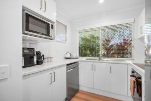 a white kitchen with white cabinets and a microwave at Renovated 2 Bedroom Ground Level Villa in Noosaville in Noosaville