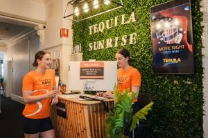 two women in orange shirts standing at a counter at Tequila Sunrise Hostel Adelaide in Adelaide