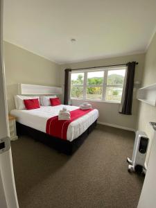 a bedroom with a bed with red pillows and a window at Rehutai Beach House in Paihia
