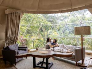 two women sitting on a couch in front of a large window at Tropical Escape Domes in Guápiles