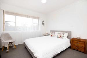 a white bedroom with a bed and a window at Rennies Beach Escape "Carinya" in Ulladulla