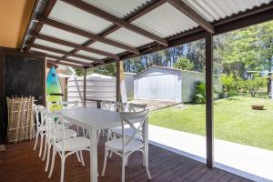 a patio with a white table and chairs and a surfboard at Sandy's Beach Shack at Bawley in Bawley Point +8 photos