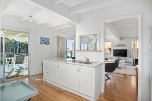 a white kitchen with a sink and a living room at MeNo's at Bawley in Bawley Point