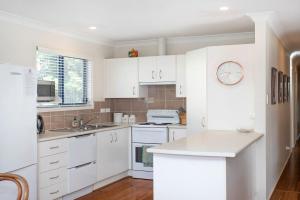 a kitchen with white cabinets and a clock on the wall at Bawley Beach Bungalow in Bawley Point