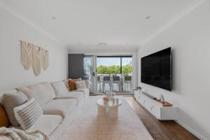 a white living room with a couch and a tv at Sanctuary Splash Getaway in Sanctuary Point
